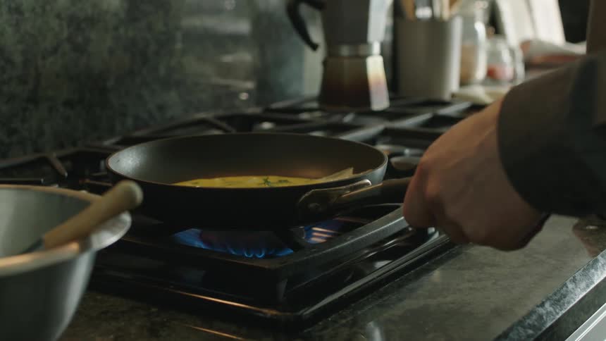 Hands of a person stirring eggs and placing them in a frying pan with heat on