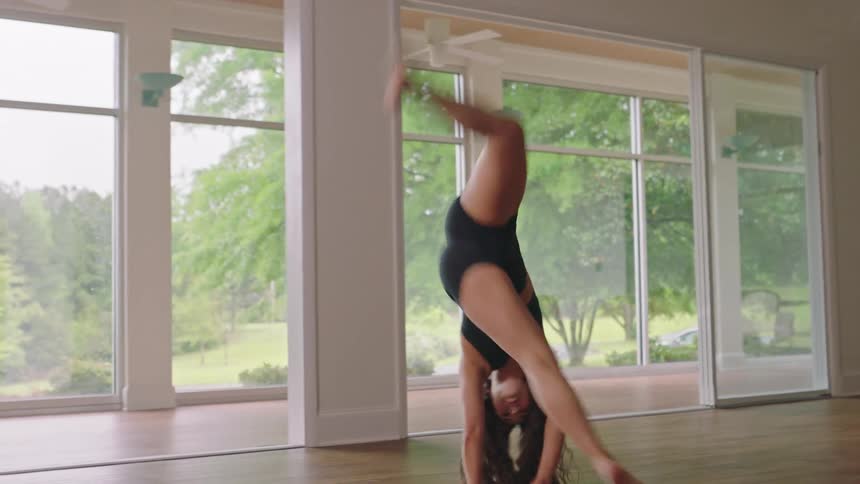 A woman in an empty room does a cartwheel that finished with her sitting on the floor in perfect form