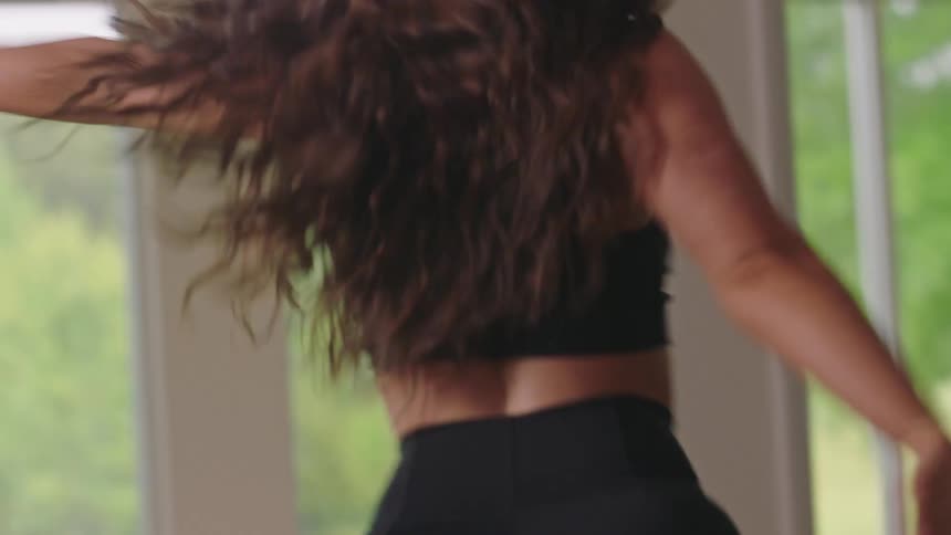 A young energetic woman wearing black sports clothes dances in a studio with large windows