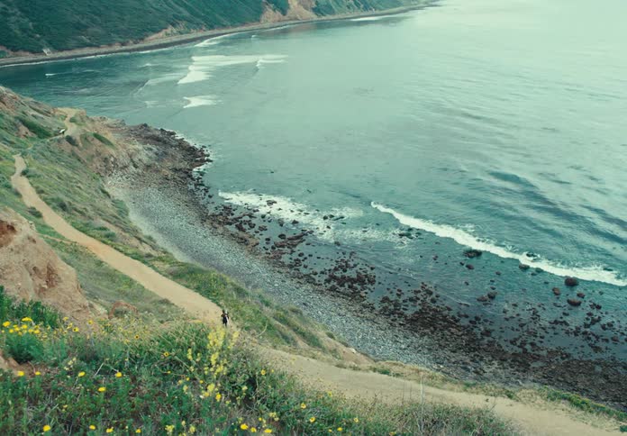Landscape seen from above the ocean with waves reaching the shore and a person walking