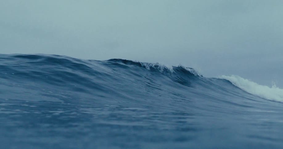 An ocean wave breaking against the beach on a cloudy day