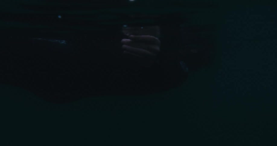 Hand bobs underwater as person floats clothed in clear water