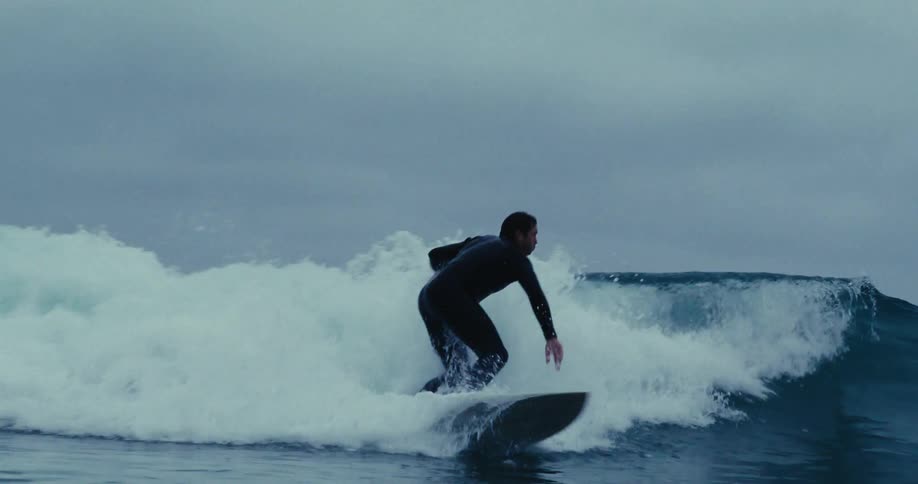 A man surfing small waves near the coast at dusk