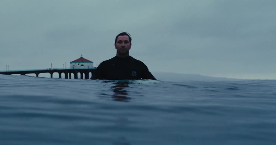 A man wearing a swimsuit stands in the water on the beach on a cloudy day