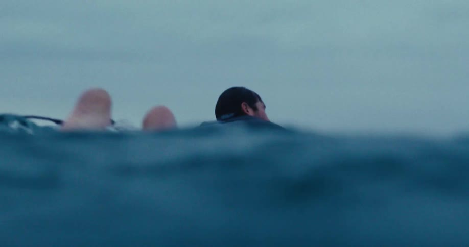 A surfer swimming over a surfboard in the ocean at dusk