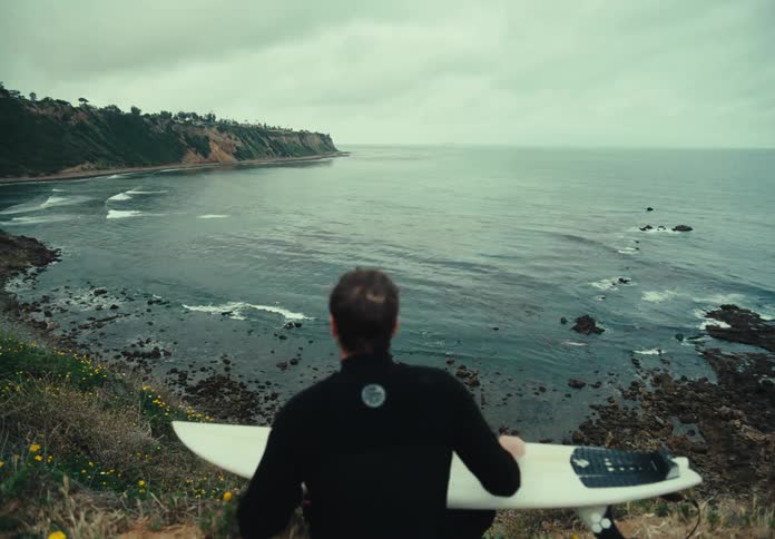 A surfer polishes a surfboard on a coast