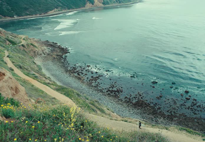 Surfer going down a slope towards the beach with his board