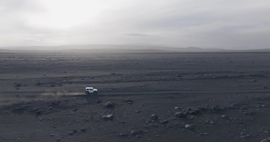Aerial panorama of a white vehicle traveling on a natural desert dirt road in a morning sky