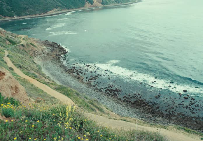 Top view of a calm beach and a person in the background with a surfboard walking