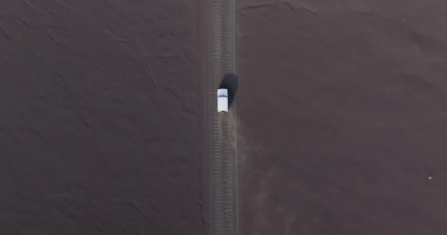 An aerial view of a white car driving on a sandy road