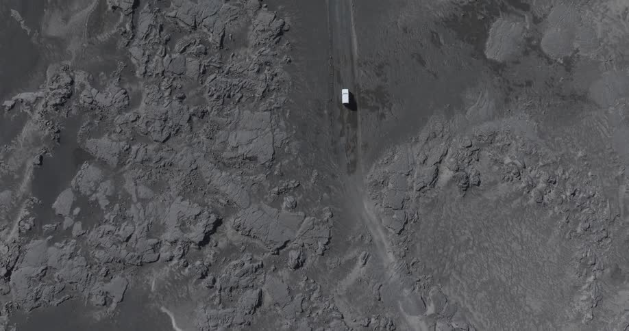 Aerial panorama of a white vehicle traveling across grayish natural soil