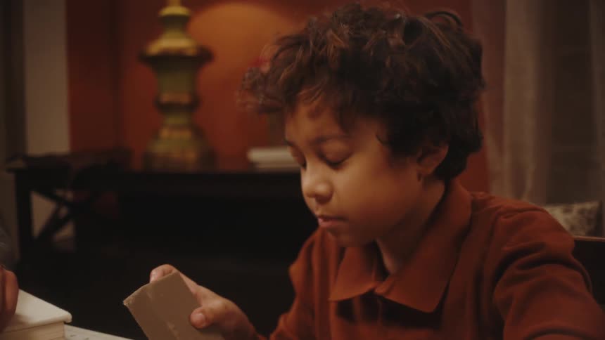 A little boy is sitting on a chair and is assembling paper airplanes