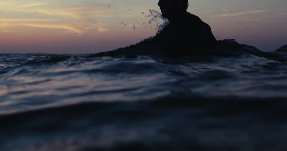 A surfer floating in the ocean at sunset