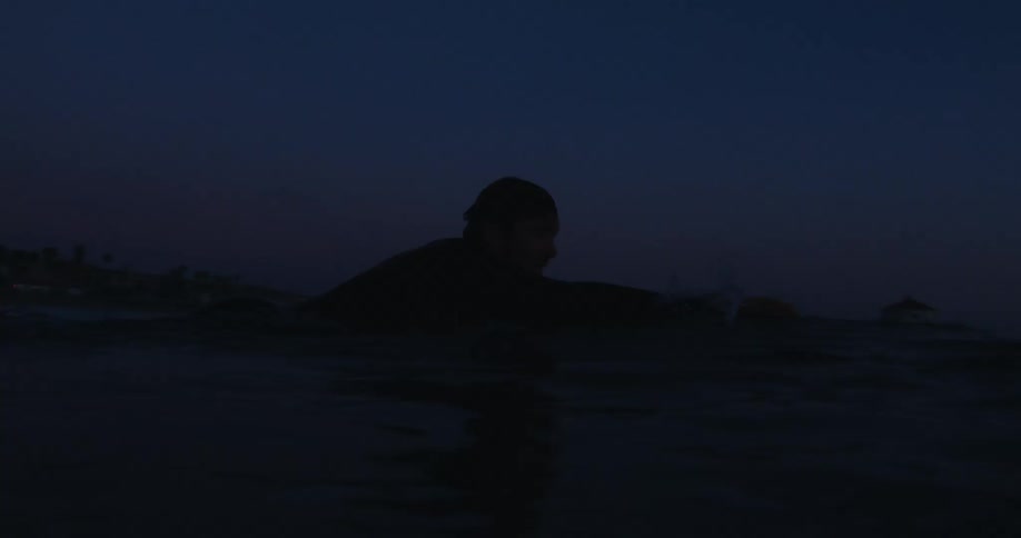 Silhouette of a surfer swimming in the ocean at night