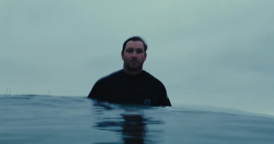 A surfer floats on the ocean under an overcast sky