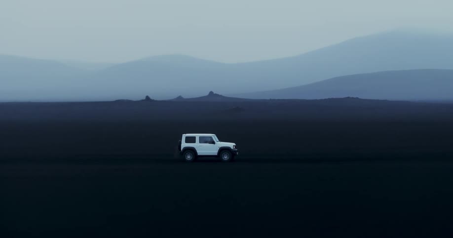 A white vehicle drives through a barren volcanic landscape