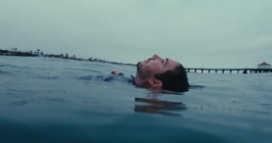 A man in a swimsuit floats on his back in the sea by the beach
