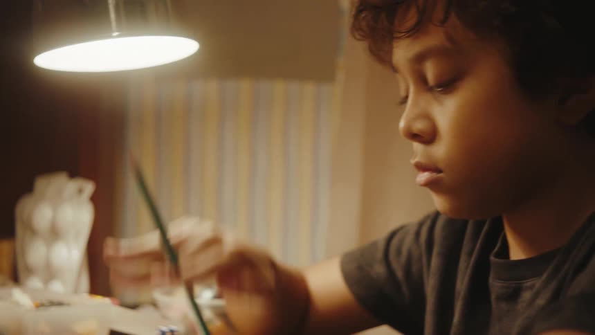 Little boy sitting at a table doodling on a blank sheet of paper