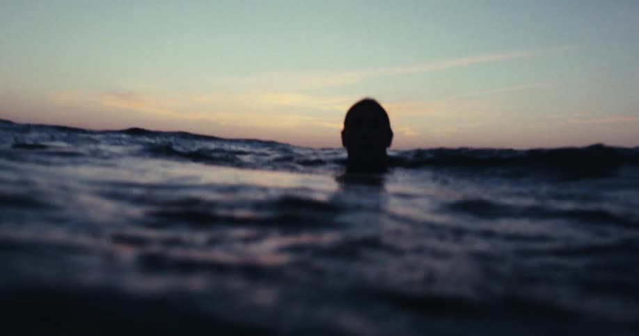 Silhouette of a man sitting on his surfboard in the middle of the sea one morning