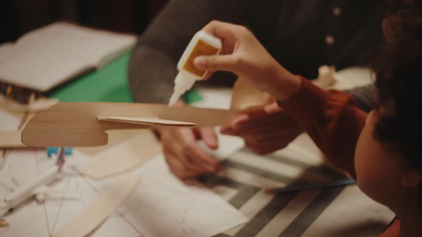 An adult helps teach a kid how to glue a balsa airplane