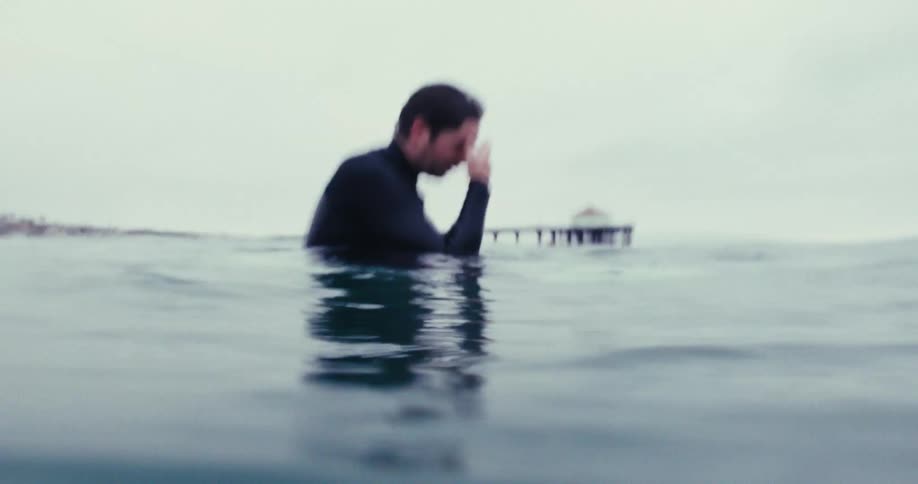 A surfer floating on a surfboard in the ocean near the coast