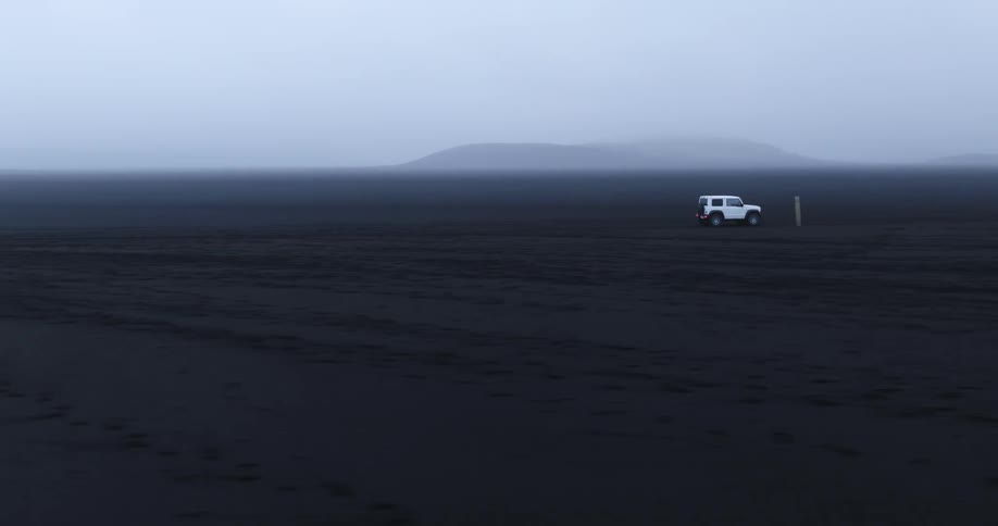 White jeep traveling across the desert with a mountain in the distance under a foggy sky