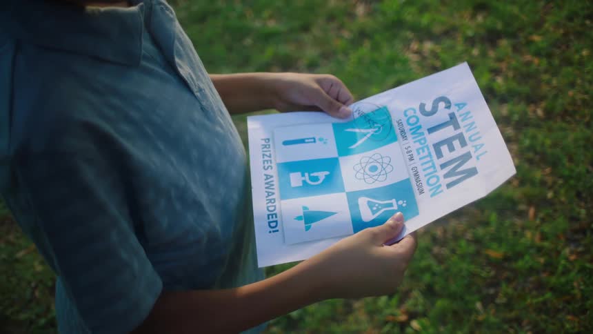 A boy holding a flyer for an annual stem competition outdoors