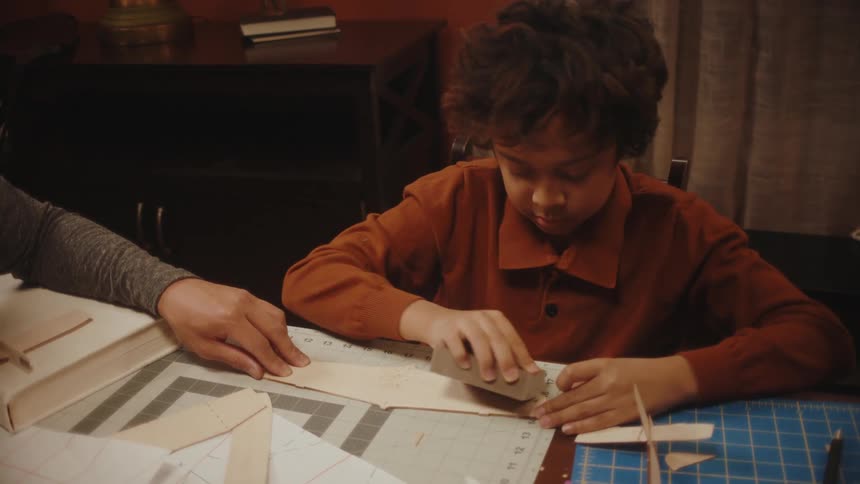 A boy sanding down and smoothing the edges of a wooden piece of a model airplane
