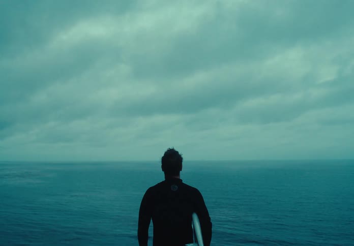 Surfer carrying his surfboard looking out to the ocean below