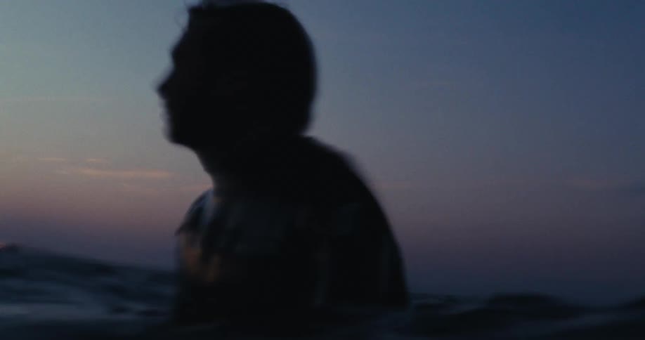 Silhouette of a man in the middle of the sea with his surfboard on a morning with a purple sky