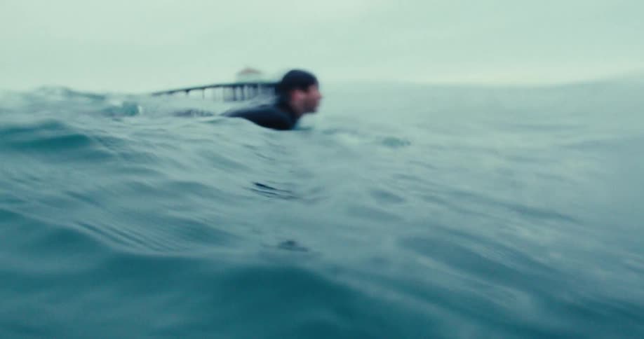 A surfer swimming in the sea trying to catch a wave