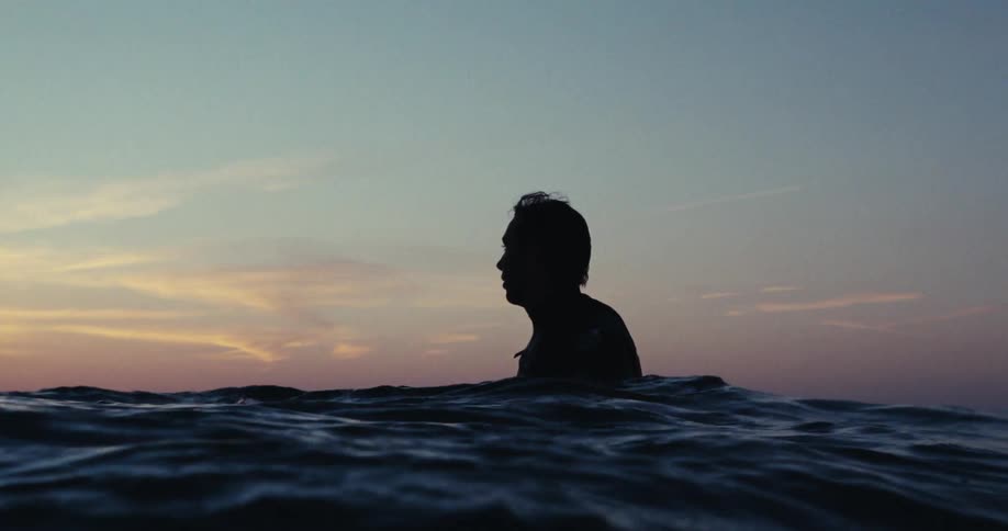 Silhouette of a man sitting over a surfboard in the ocean at sunset