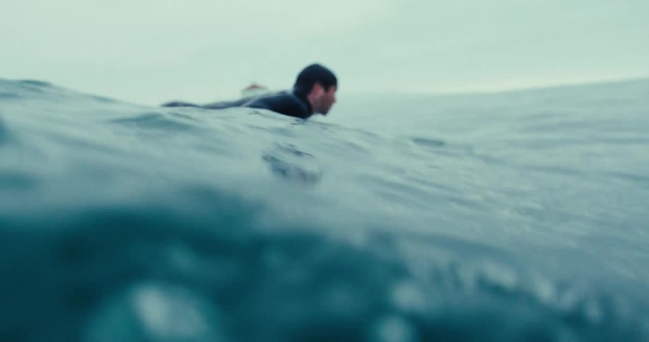 A man is paddling in the ocean looking for a wave