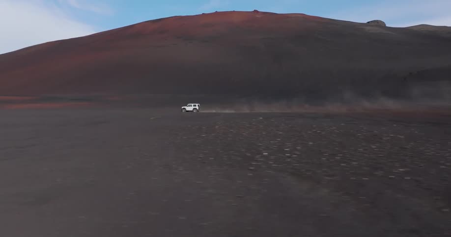 A white jeep moving across a barren landscape with rocky ground and rolling hills