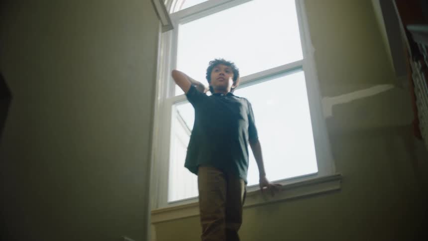 A boy throwing a paper plane from a staircase at home