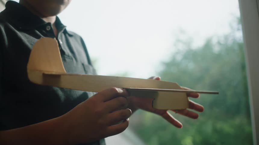 A boy playing with a balsa wood plane near a window