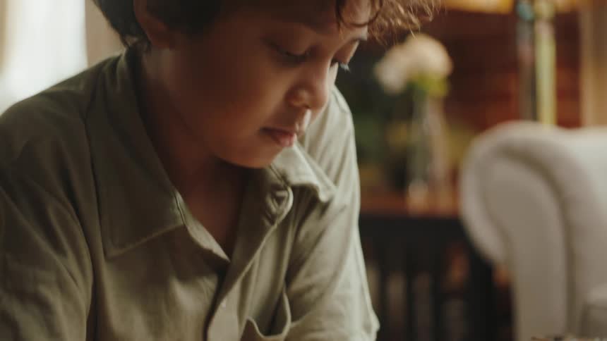 Boy writing with pen and paper on the living room at home