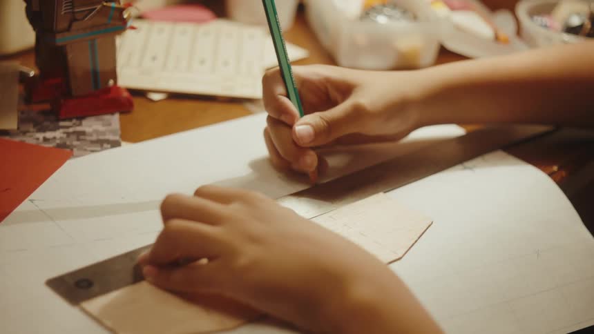 Hands of a boy drawing a straight line on a piece of paper with the help of a ruler