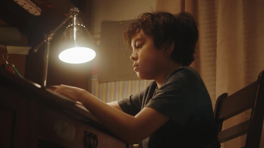 A boy sitting in a chair making drawings surrounded by discarted papers all over the floor