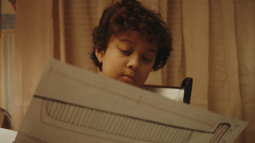 A boy holding a paper blueprint in his room