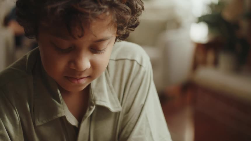 Boy with curly hair and a green shirt scratches on a piece of paper resting on a coffee table