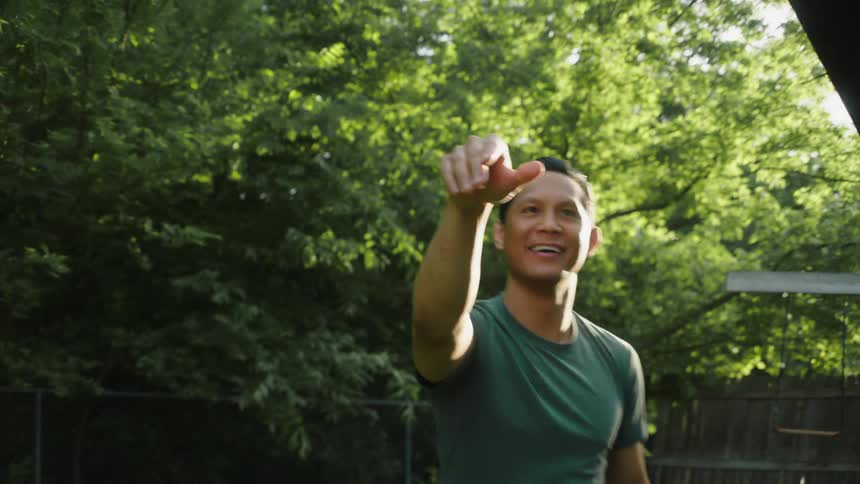 A happy man wearing a green tshirt throws a wooden airplane and laughs in the yard