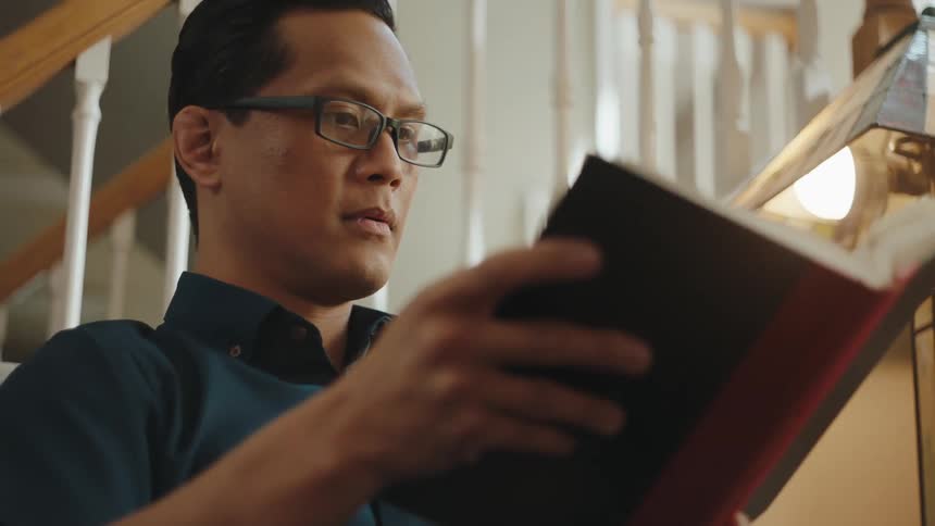 A man sitting on a cozy room reading a book