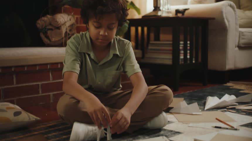 Boy sitting on the carpet at home using a compass and with leaves and papers around him