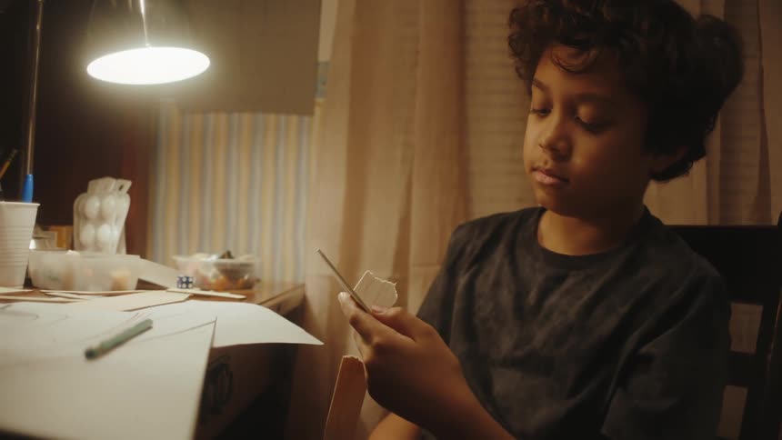 Portrait of a boy sitting down feeling discouraged as he tries to assemble a piece of cardboard that he ends up throwing on the table