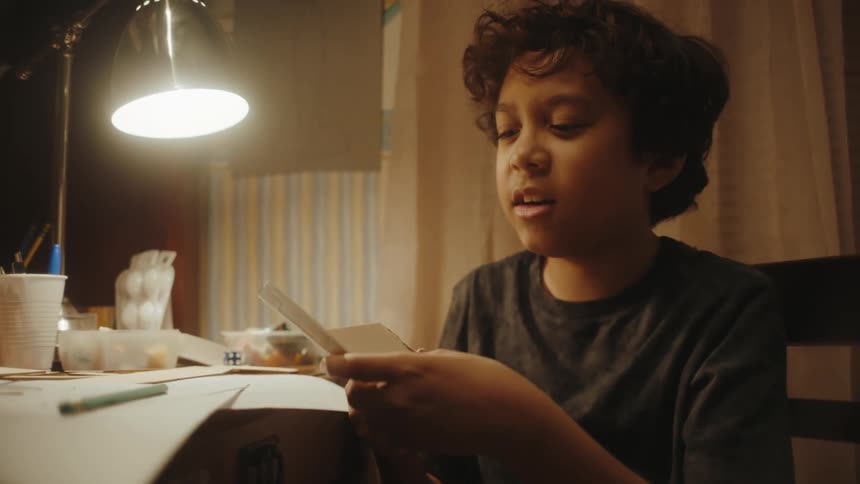 Boy sitting on a chair breaking a cardboard in half and looking discouraged
