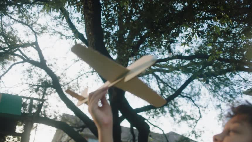 Child with curly hair plays with a wooden airplane in the yard