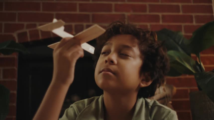 A boy looking at a toy paper plane in the living room