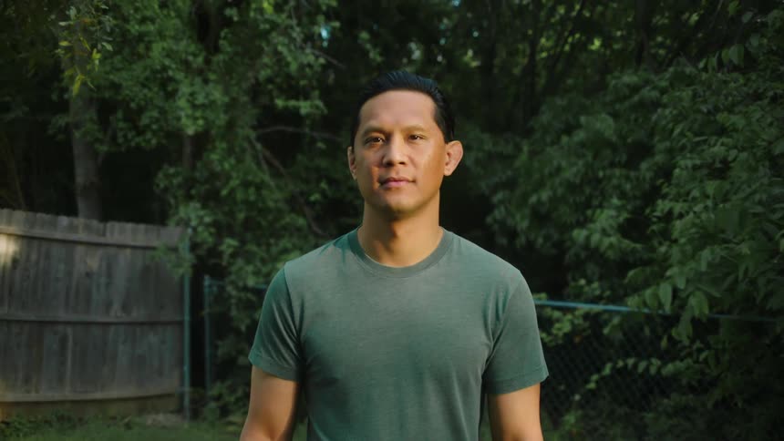 A portrait of a man in a green tshirt smiling in a green yard