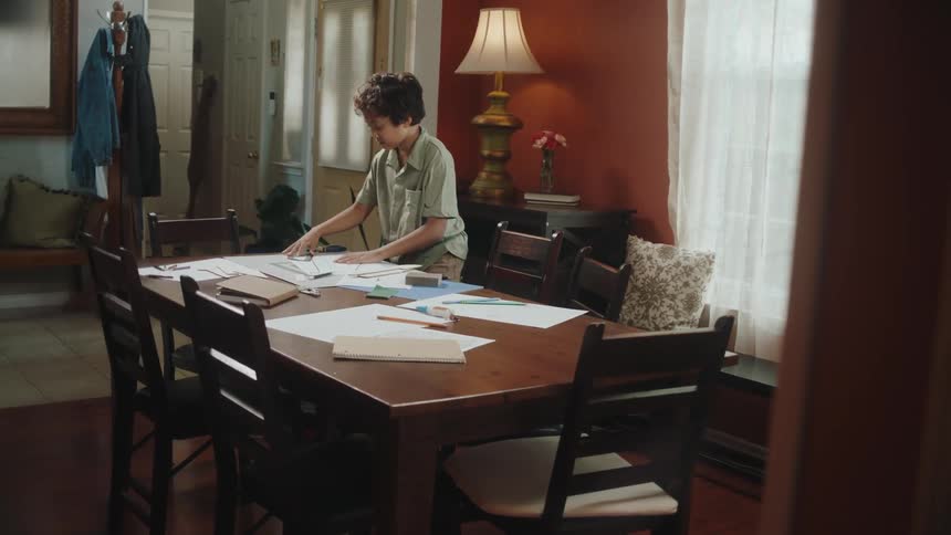 Boy arriving in the room taking off his backpack and working on a project with a ruler on the table